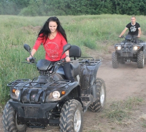 Esiplaanil punase särgiga neiu sõitmas musta ATV-ga, tagaplaanil noormees sõitmas ATV-ga.